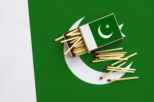 Pakistan flag  is shown on an open matchbox, from which several matches fall and lies on a large flag photo