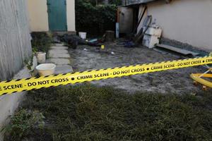 Victim of a violent crime in a backyard of residental house in evening. Dead man body under the yellow police line tape and evidence markers on crime scene photo