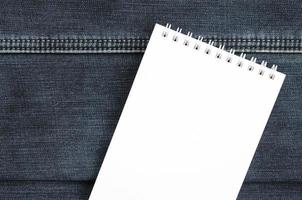 White notebook with clean pages lying on dark blue jeans background. Image with copy space photo