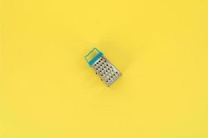 Stainless steel grater lies on a pastel colored paper. Kitchen accessories. Tools for cooking. Flat lay top view photo