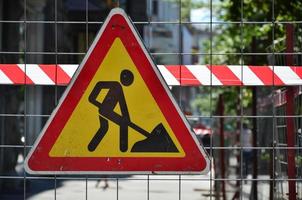 The warning sign under construction is attached to a metal mesh fence with a red and white striped signal tape photo