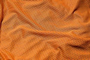 Sport clothing fabric texture background. Top view of orange polyester nylon cloth textile surface. Colored basketball shirt with free space for text photo