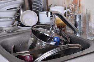 A huge pile of unwashed dishes in the kitchen sink and on the countertop photo