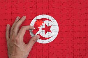 Tunisia flag  is depicted on a puzzle, which the man's hand completes to fold photo