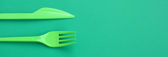 Disposable plastic cutlery green. Plastic fork and knife lie on a green background surface photo