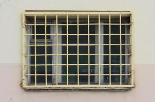 The texture of the wall of a residential building with a window that is protected by a metal grill. Old method of protecting housing from robbers photo