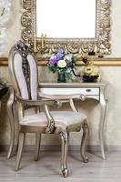 A fragment of a retro interior with a chair and table, on which is a telephone and a vase of flowers. Above the table hangs an empty picture frame for your photo