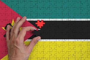 Mozambique flag  is depicted on a puzzle, which the man's hand completes to fold photo