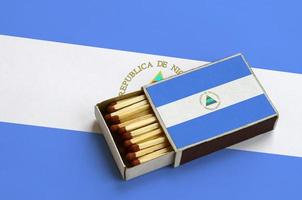 Nicaragua flag  is shown in an open matchbox, which is filled with matches and lies on a large flag photo