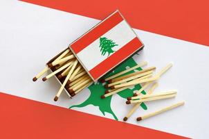 la bandera de líbano se muestra en una caja de cerillas abierta, de la que caen varias cerillas y se encuentra en una bandera grande foto