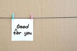 Good for you. Note is written on a white sticker that hangs with a clothespin on a rope on a background of brown cardboard photo
