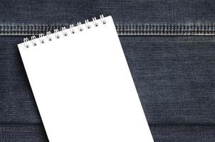 White notebook with clean pages lying on dark blue jeans background. Image with copy space photo