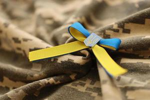 TERNOPIL, UKRAINE - SEPTEMBER 2, 2022 Ribbon with Ukrainian Coat of Arms and national flag colors on army camouflage uniform photo