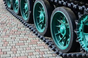 A military vehicle on caterpillar tracks stands on a square of paving stones. Photo of green caterpillars with metal wheels that rotate them