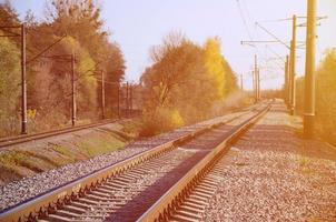 Autumn industrial landscape. Railway receding into the distance among green and yellow autumn trees photo