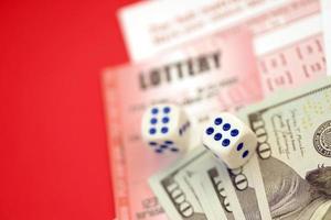 Red lottery ticket with dice and money lies on pink gambling sheets with numbers for marking to play lottery. Lottery playing concept or gambling addiction. Close up photo