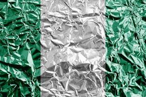 Nigeria flag depicted in paint colors on shiny crumpled aluminium foil closeup. Textured banner on rough background photo