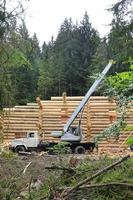 el proceso de construcción de una casa de madera a partir de vigas de madera de forma cilíndrica. grúa en condiciones de trabajo foto