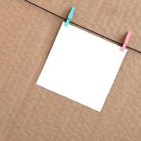 White blank card on rope on a brown cardboard background. Creative reminder, small sheet of paper on wooden clothespin, memo backdrop photo