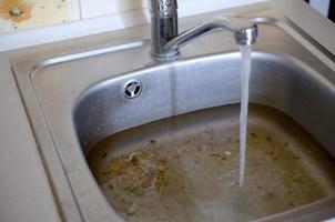 tapón del fregadero de acero inoxidable cerca del orificio lleno de agua y partículas de comida foto