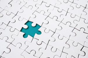 Close-up texture of a white jigsaw puzzle in assembled state with missing elements forming a blue pad for text. Copy space photo