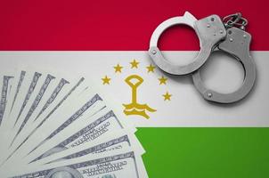 Tajikistan flag  with handcuffs and a bundle of dollars. The concept of illegal banking operations in US currency photo