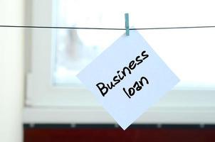 Business loan. Note is written on a white sticker that hangs with a clothespin on a rope on a background of window glass photo