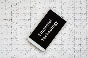 A modern big smartphone with a touch screen lies on a white jigsaw puzzle in an assembled state with inscription. Financial technology photo