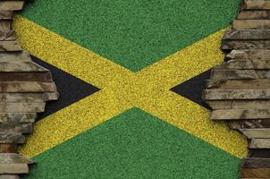 Jamaica flag depicted in paint colors on old stone wall closeup. Textured banner on rock wall background photo