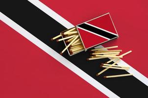 Trinidad and Tobago flag  is shown on an open matchbox, from which several matches fall and lies on a large flag photo