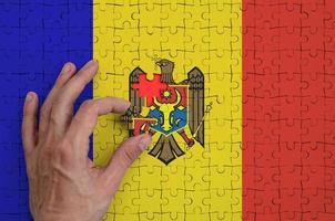 Moldova flag  is depicted on a puzzle, which the man's hand completes to fold photo