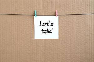 Let's talk Note is written on a white sticker that hangs with a clothespin on a rope on a background of brown cardboard photo