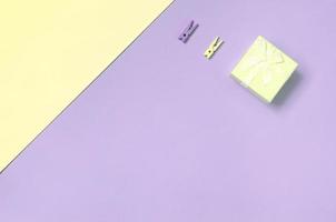 Small yellow gift box and two pegs lie on texture background of fashion pastel yellow and violet colors paper photo