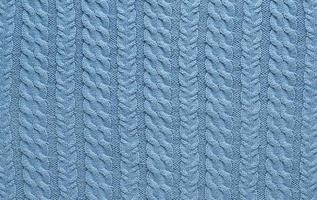 Texture of smooth knitted blue sweater with pattern. Top view, close-up. Handmade knitting wool or cotton fabric texture. Background of knitting patterns with a vertical Braid Cable. photo