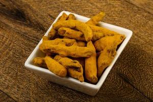 Tumeric roots in a bowl on wooden background photo