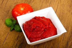 Tomato paste in a bowl on wooden background photo