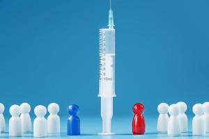 Vaccinate or refuse a syringe with a vaccine with two groups of people a red and a blue human model. photo