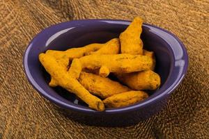Tumeric roots in a bowl on wooden background photo