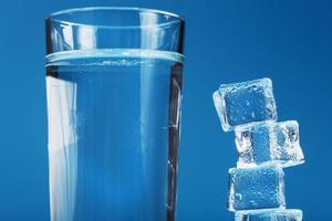 Ice cubes tower with a glass of cold and clean water on a blue background. photo