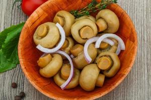 Champiñón en escabeche en un recipiente sobre fondo de madera foto