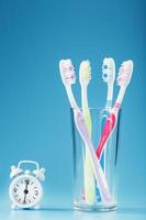 Toothbrushes of different colors in a glass with an alarm clock on a blue background. photo