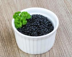 Black caviar in a bowl on wooden background photo