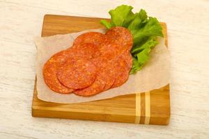 Pepperoni sausage on wooden board and wooden background photo