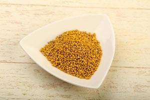 Mustard seeds in a bowl on wooden background photo