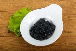 Black caviar in a bowl on wooden background photo