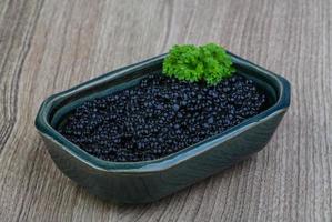 Black caviar in a bowl on wooden background photo