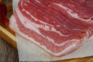 Raw bacon on wooden board and wooden background photo