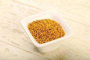 Mustard seeds in a bowl on wooden background photo