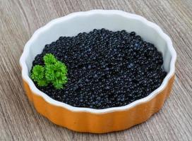 Black caviar in a bowl on wooden background photo