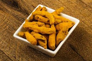 Tumeric roots in a bowl on wooden background photo
